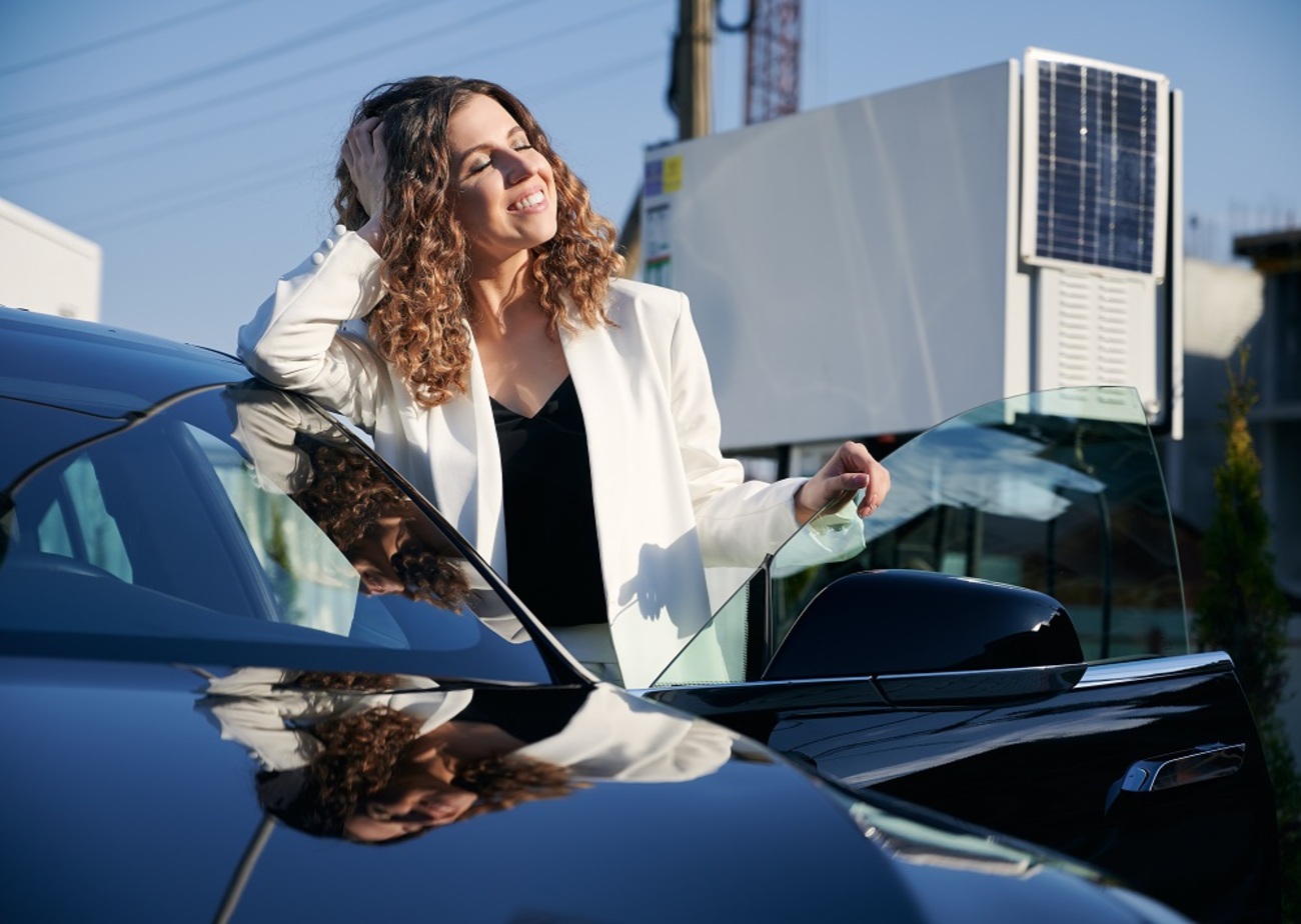 Mujer sonríe al salir de un coche un día soleado