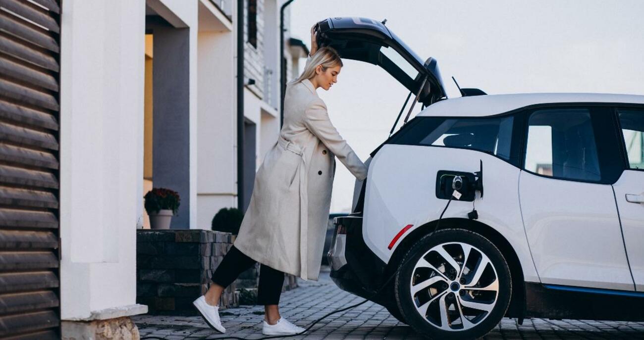 Una mujer carga su coche eléctrico / FREEPIK